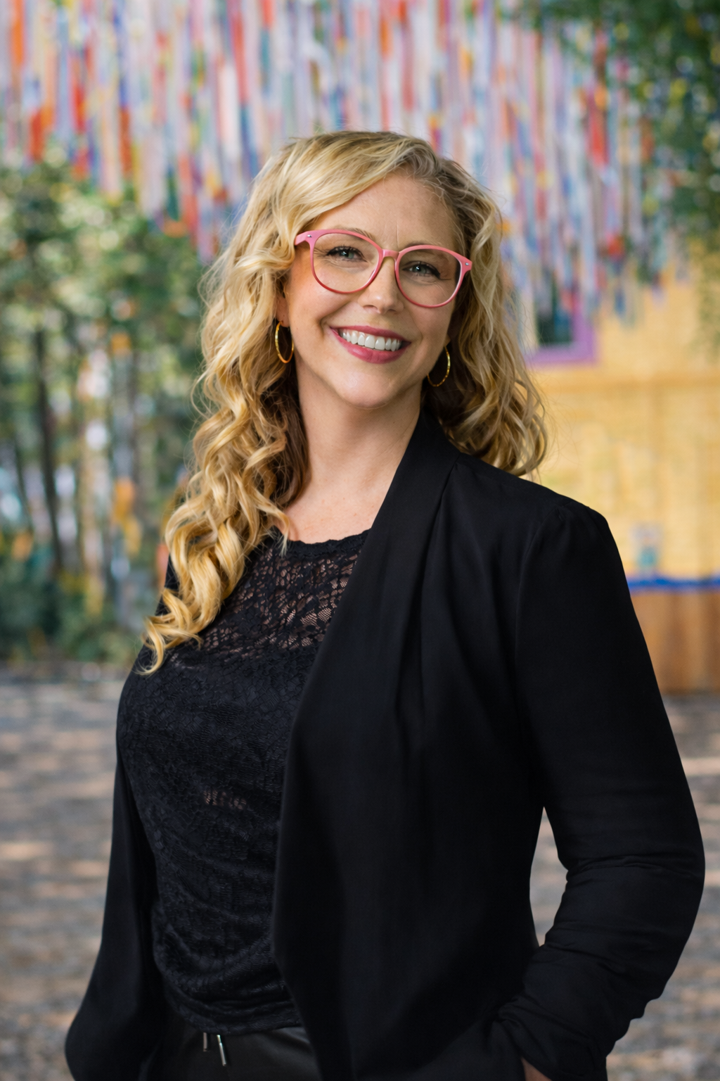 Penny Lamarre sourit face à l’objectif, portant des lunettes, un blazer noir et un haut sombre, sur fond extérieur flou.